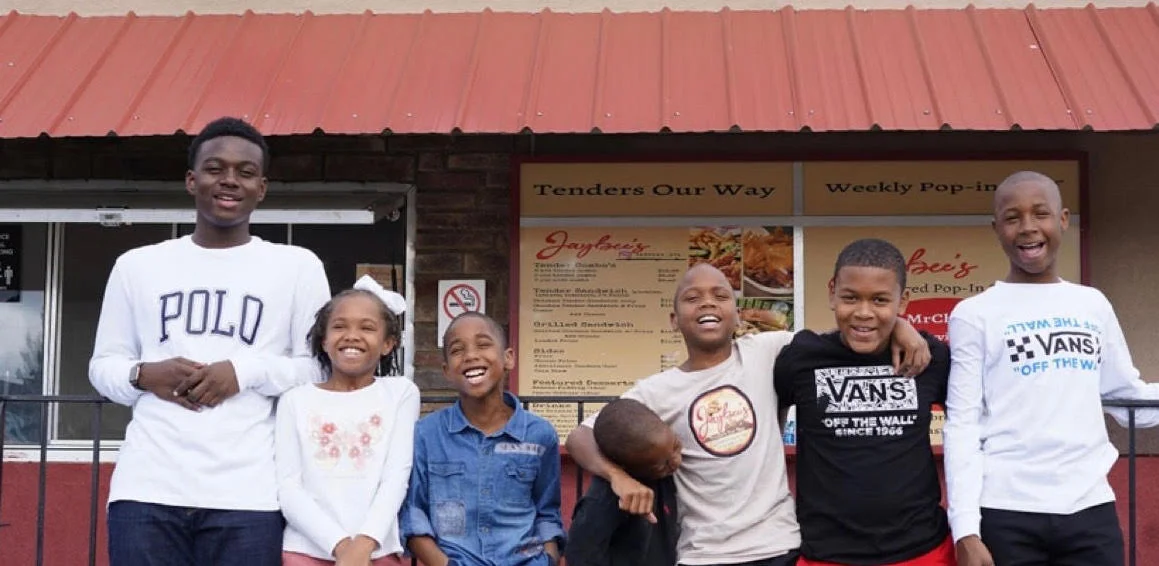 Children smiling outside a restaurant with a menu display