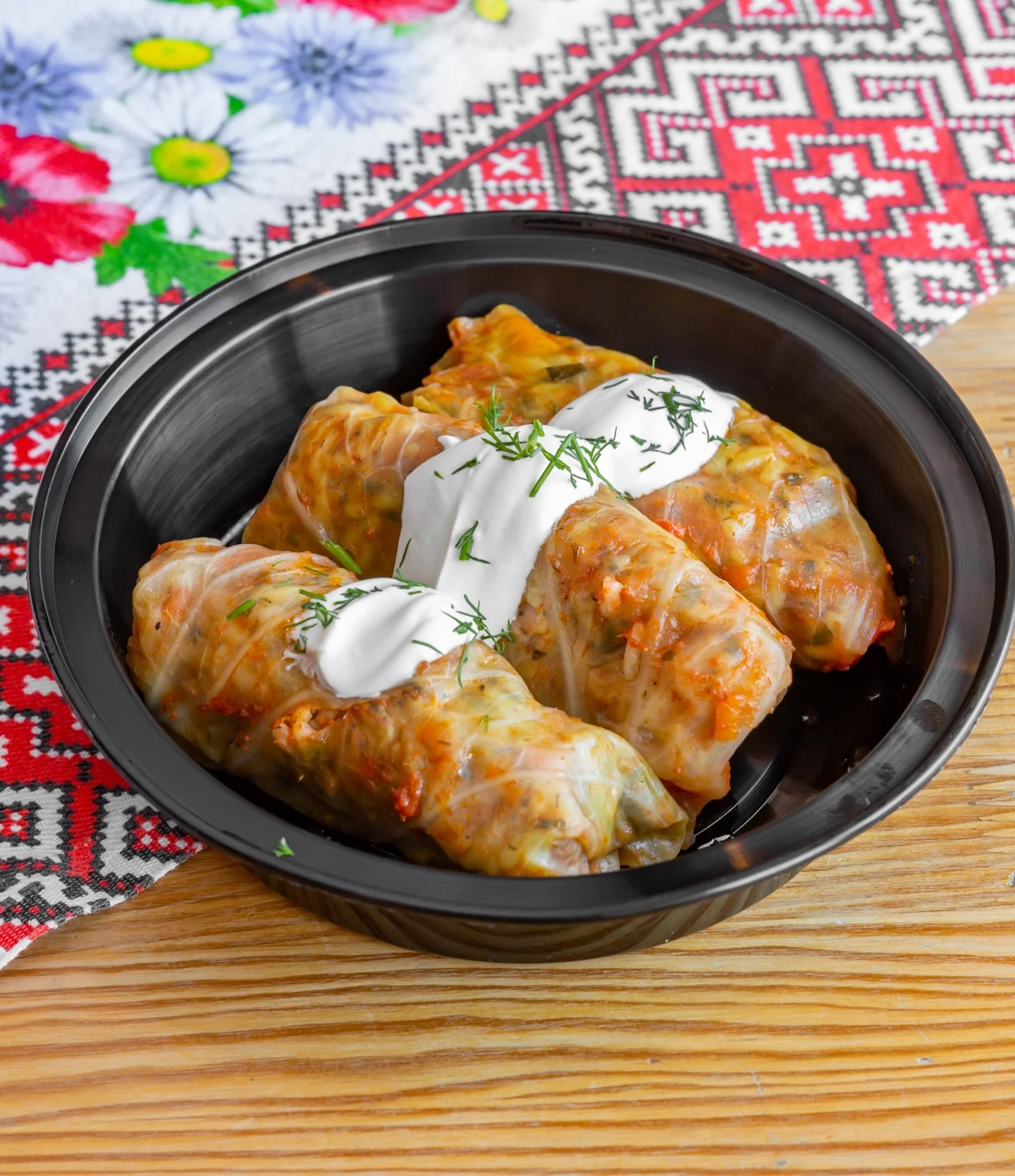 A bowl of stuffed cabbage rolls topped with sour cream and fresh herbs, placed on a decorative tablecloth.
