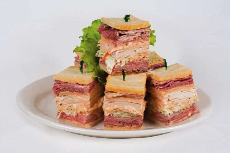 An assortment of layered sandwiches stacked together, featuring various meats and garnished with lettuce, served on a white plate.