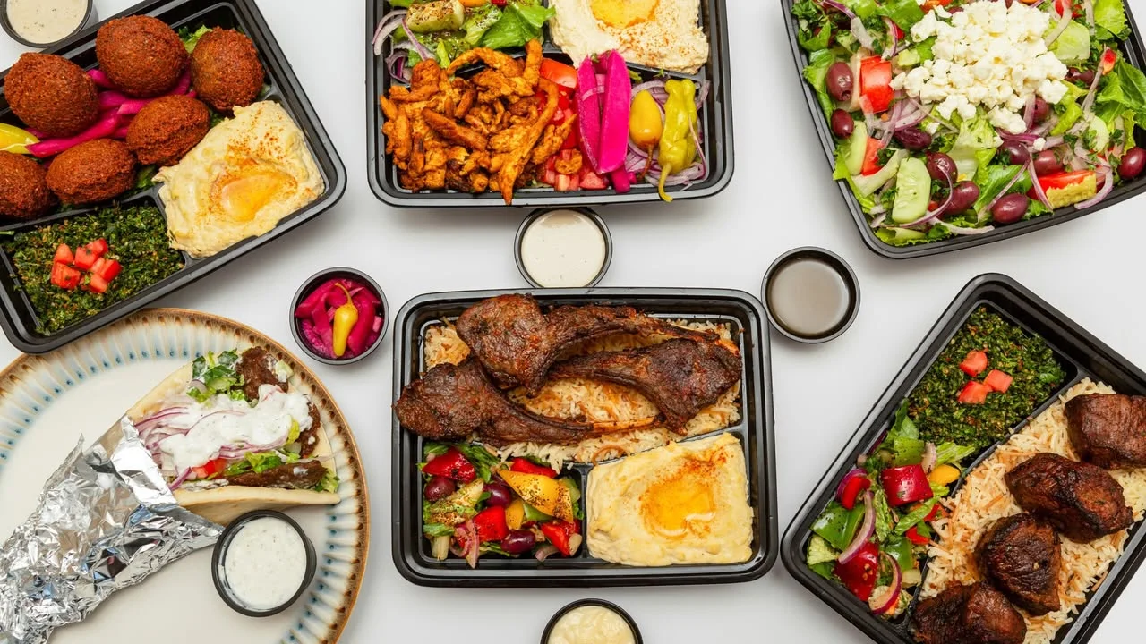A hearty meal featuring grilled meats, rice, a fresh salad with tomatoes and greens, and a side of hummus, all served on a patterned plate.