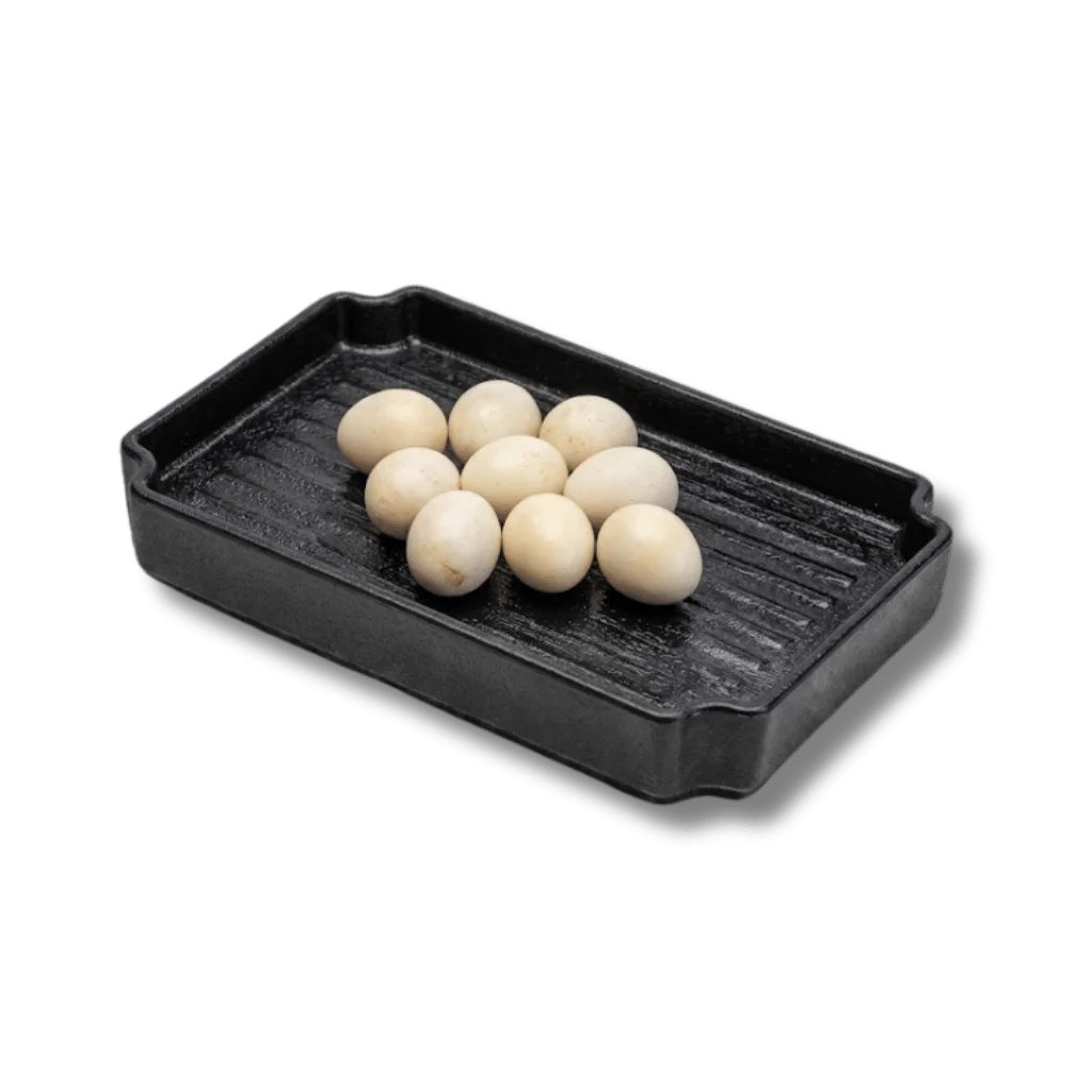 A cast iron grill pan with ten small white eggs arranged on it.