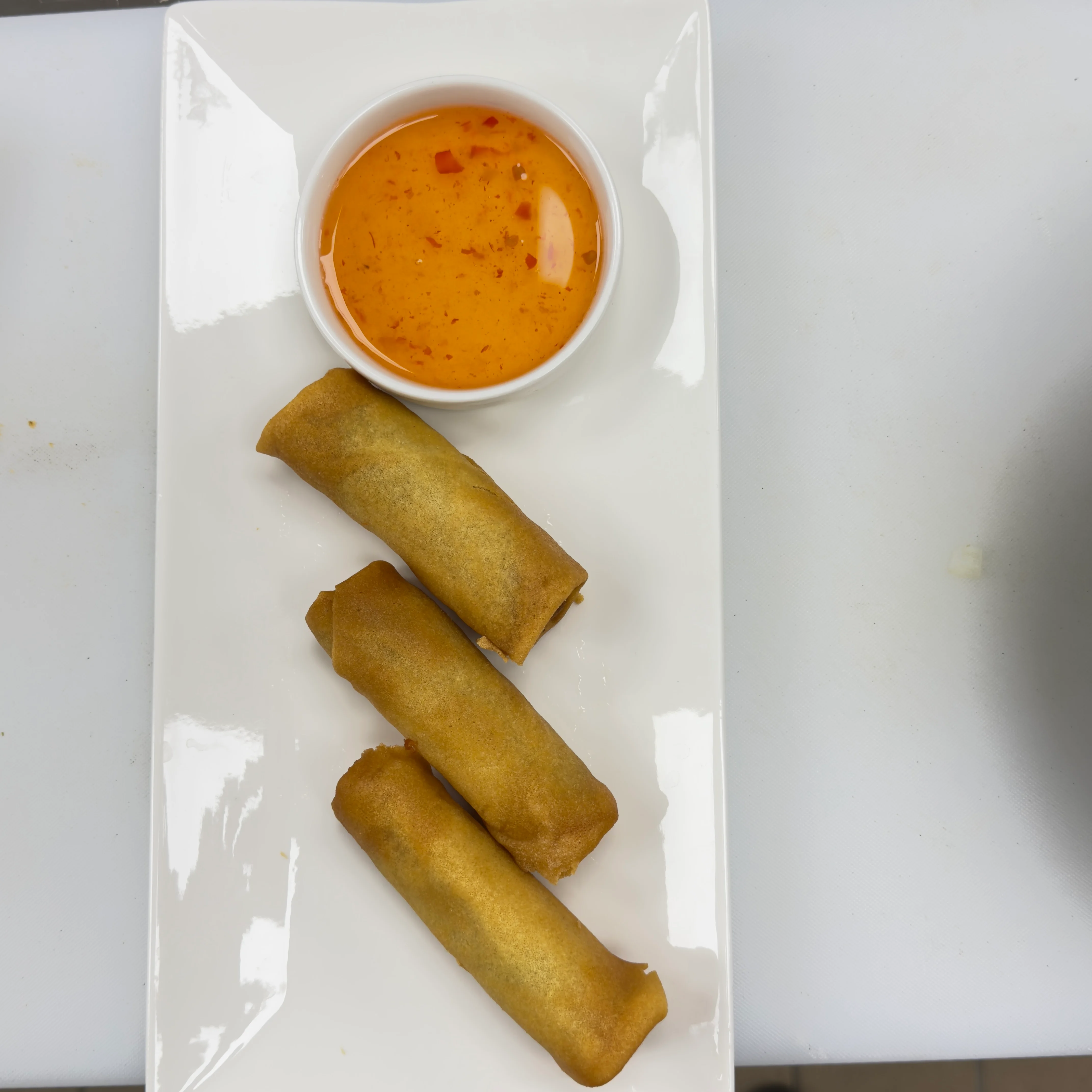 Three golden-brown spring rolls served with a small bowl of sweet chili sauce.