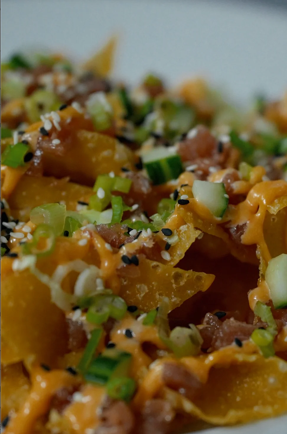 Close-up of nachos topped with sauce, green onions, and sesame seeds.