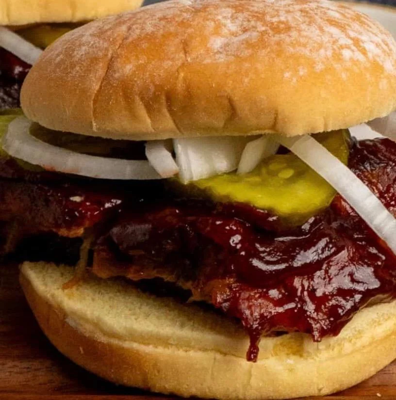 A barbecue sandwich featuring meat, pickles, and onions nestled between a soft bun.