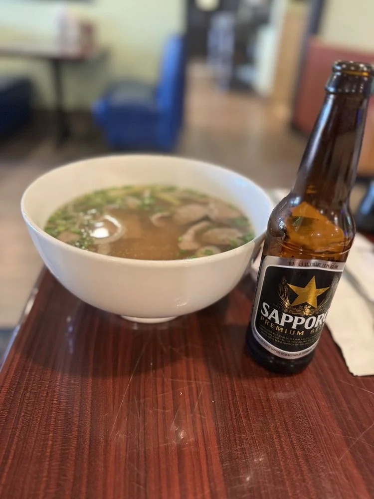 Bowl of Vietnamese pho with beef and herbs alongside a Sapporo beer