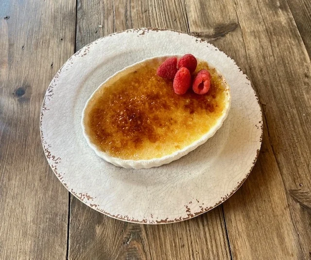 A creamy dessert with a caramelized sugar top and fresh raspberries on a rustic plate.