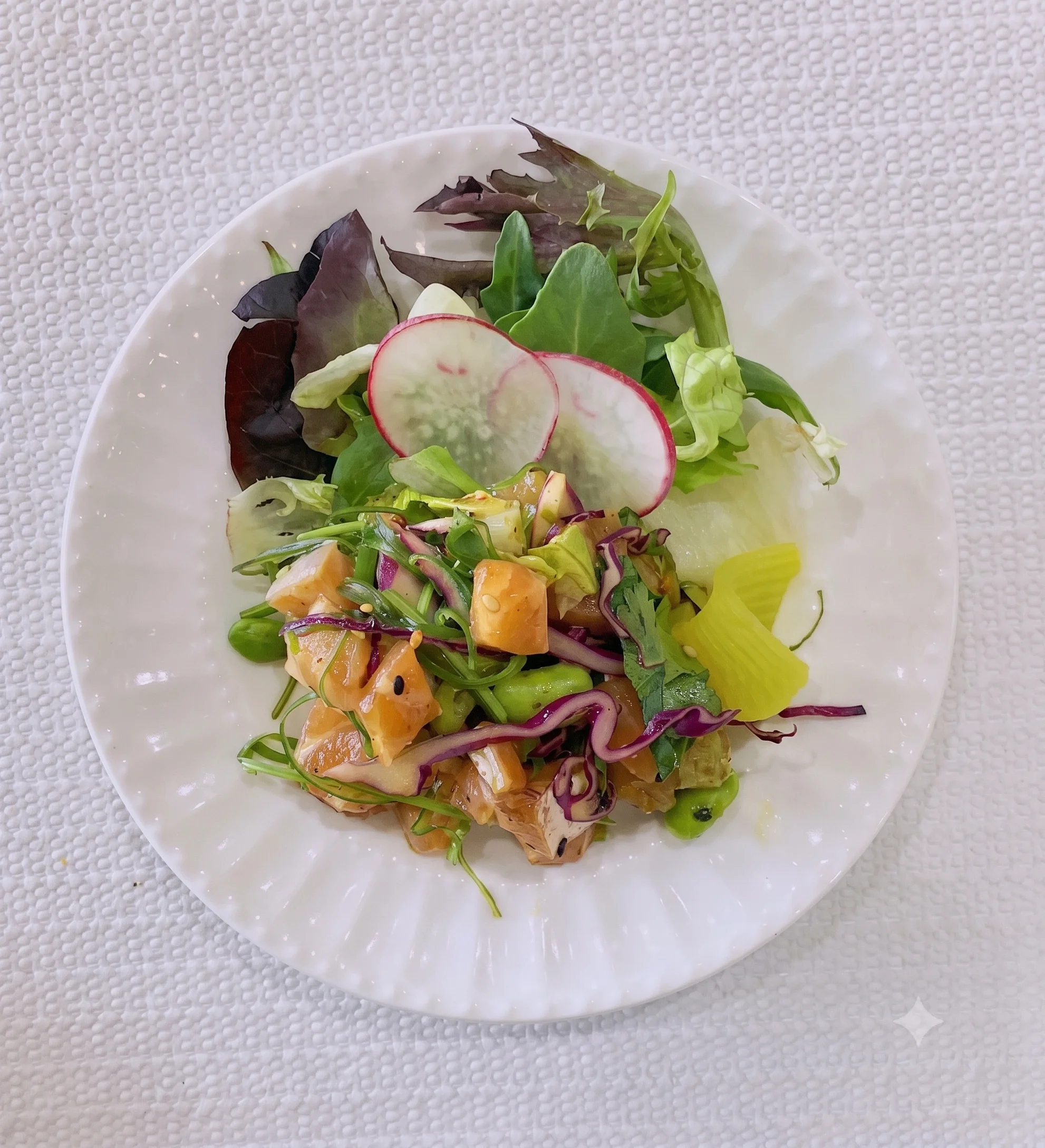 Colorful salad with mixed greens, radishes, and diced vegetables on a white plate.