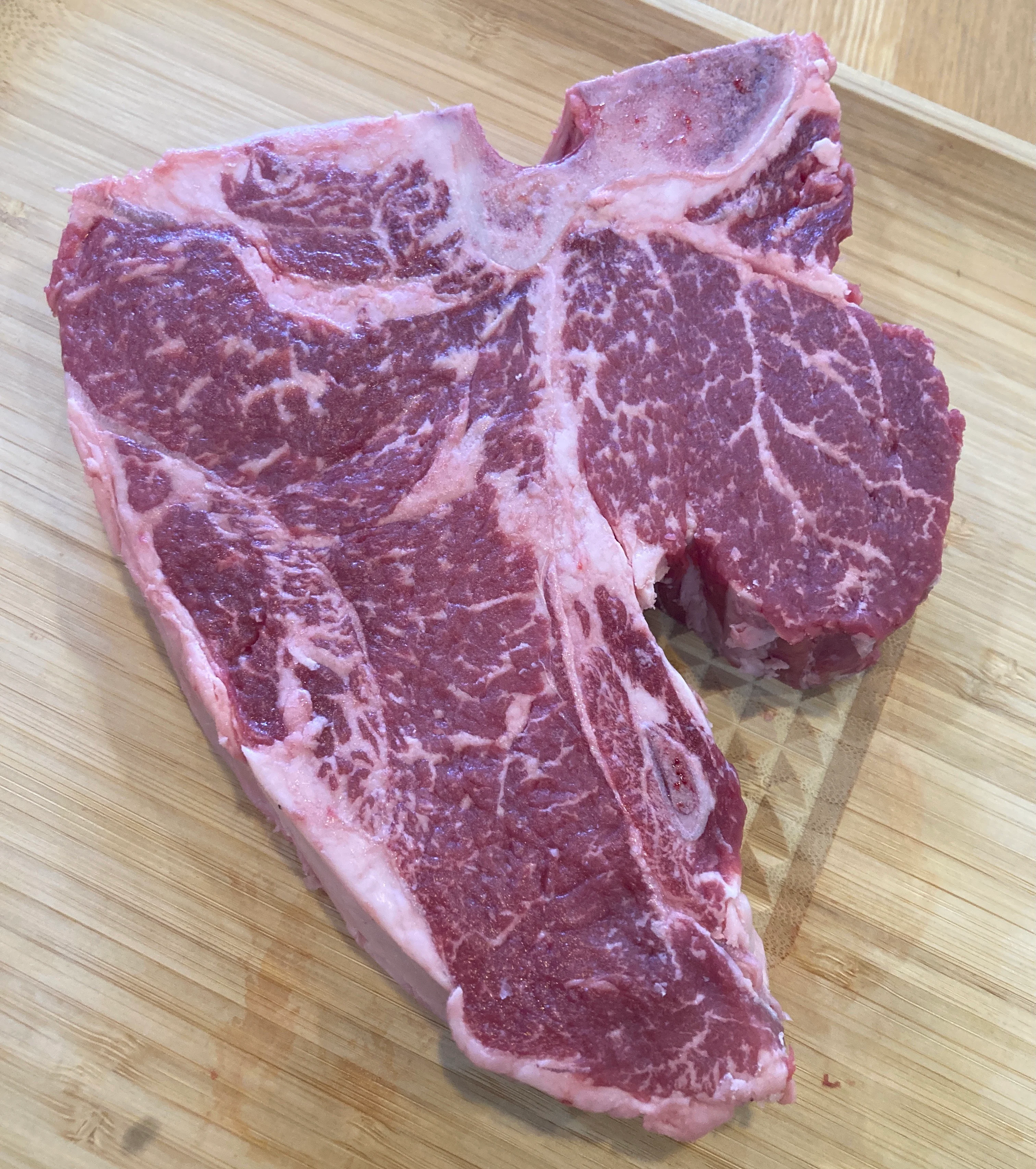 Raw T-bone steak on a wooden cutting board.