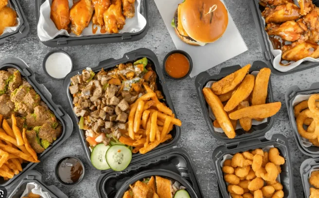 Three bowls filled with rice, meat, lettuce, and sauces, accompanied by pita bread and several packets of hot sauce, sitting on a red surface.