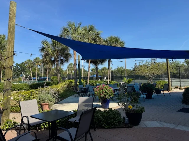 Outdoor dining area with palm trees and blue shade sails