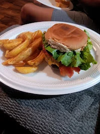 A sandwich with lettuce, bacon, and cheese, accompanied by several potato wedges on a disposable plate.