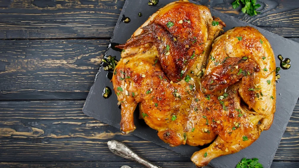 A roasted chicken garnished with herbs, resting on a dark platter.
