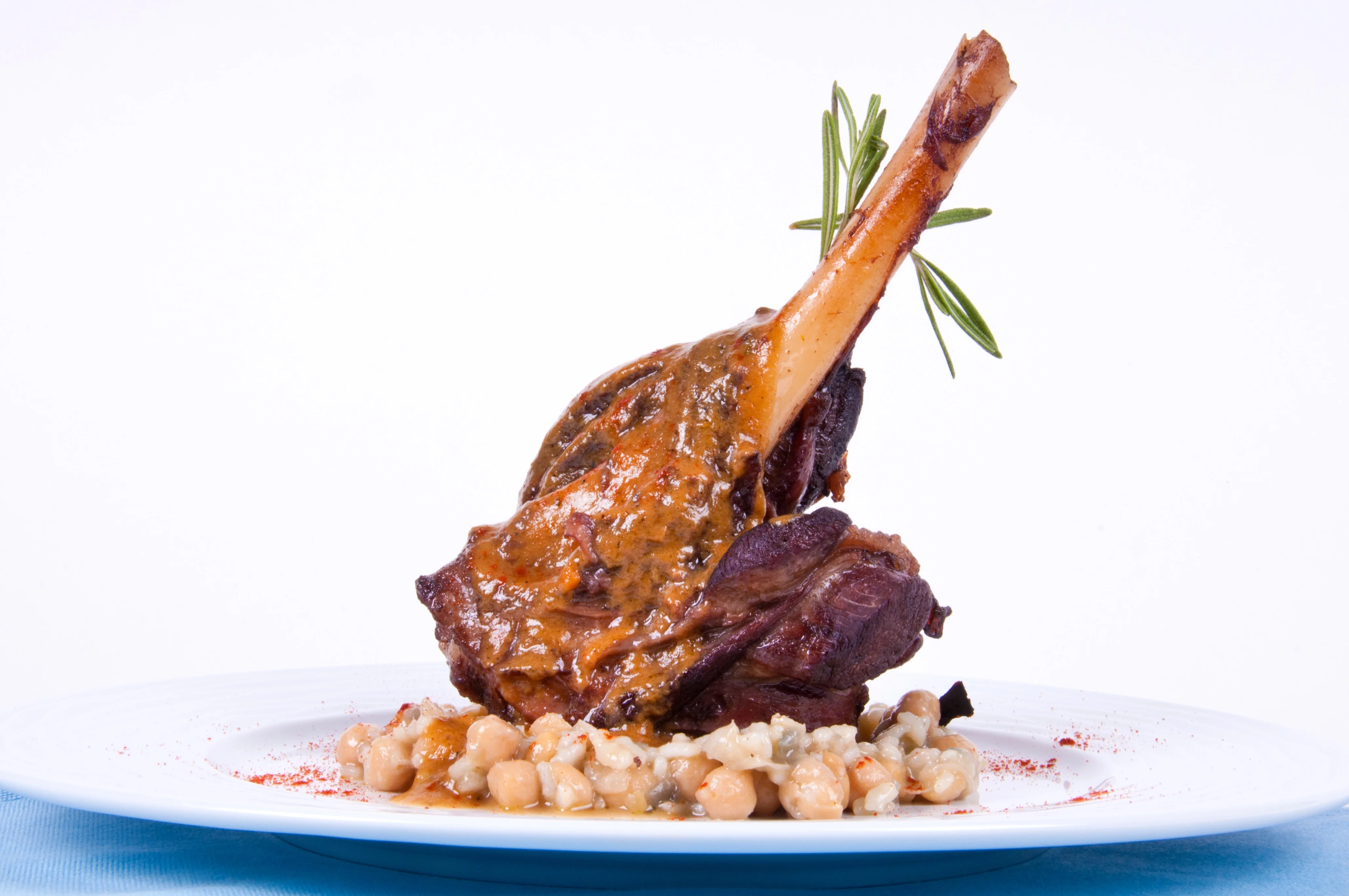 A succulent lamb shank served on a plate with a savory sauce, garnished with rosemary, resting on a bed of chickpeas and grains.