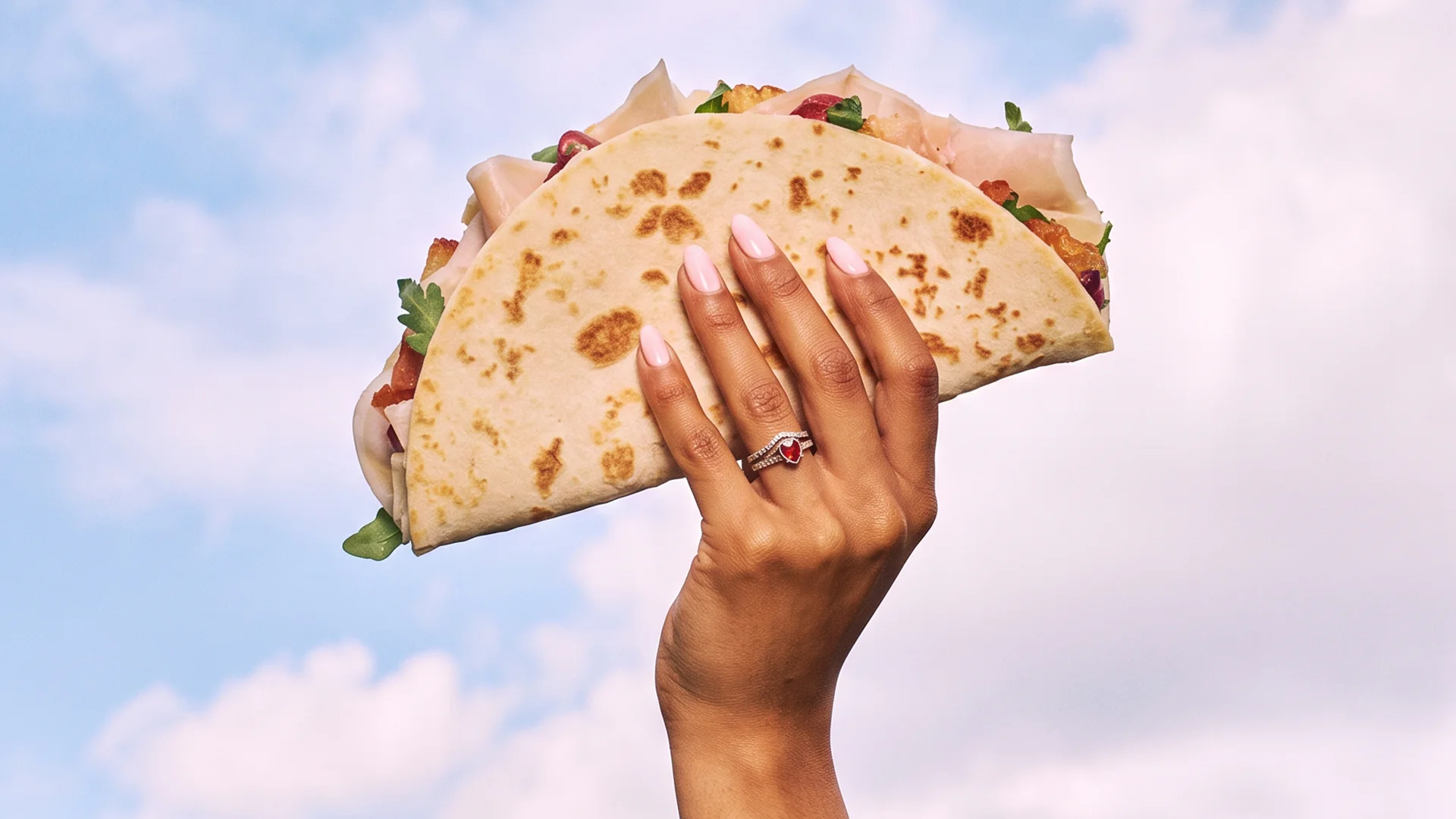 Hand holding a red packaging with tear strip against a blue sky