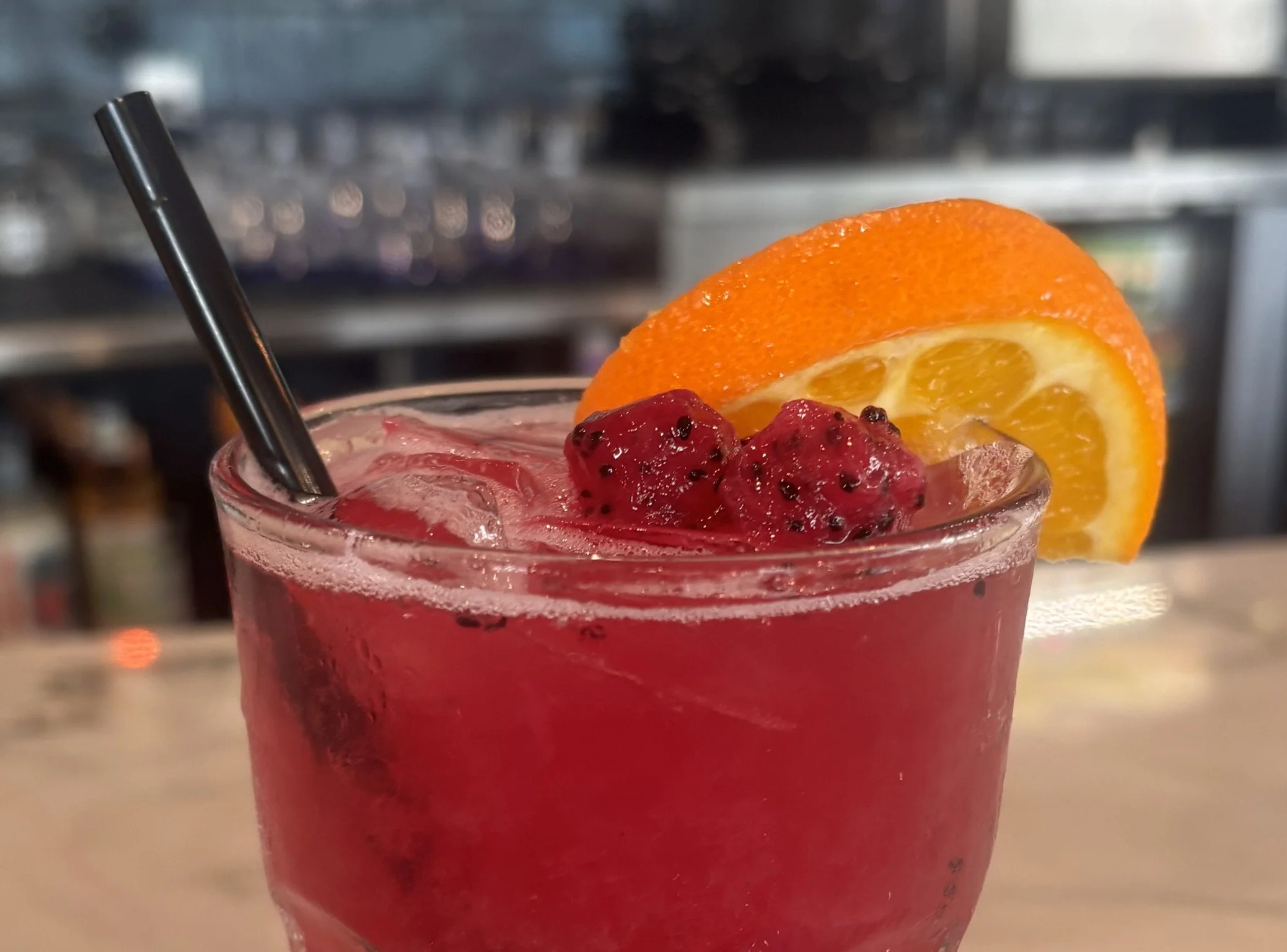 Colorful cocktail with orange slice and raspberries on a bar counter.