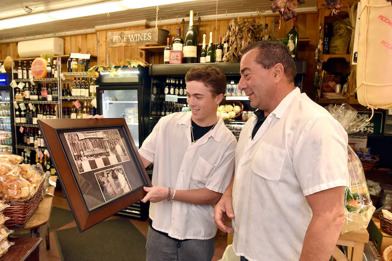 Two men sharing a framed photo in a rustic grocery store