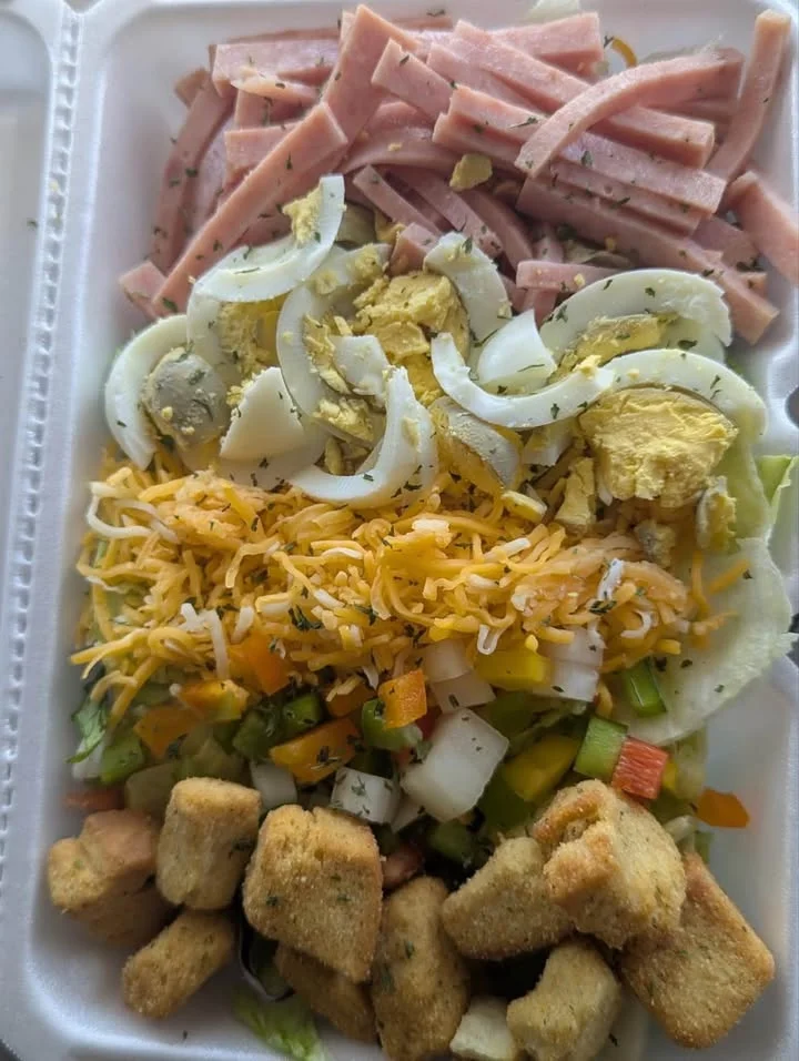 A colorful salad featuring diced ham, onions, eggs, shredded cheese, and assorted vegetables served in a tray.