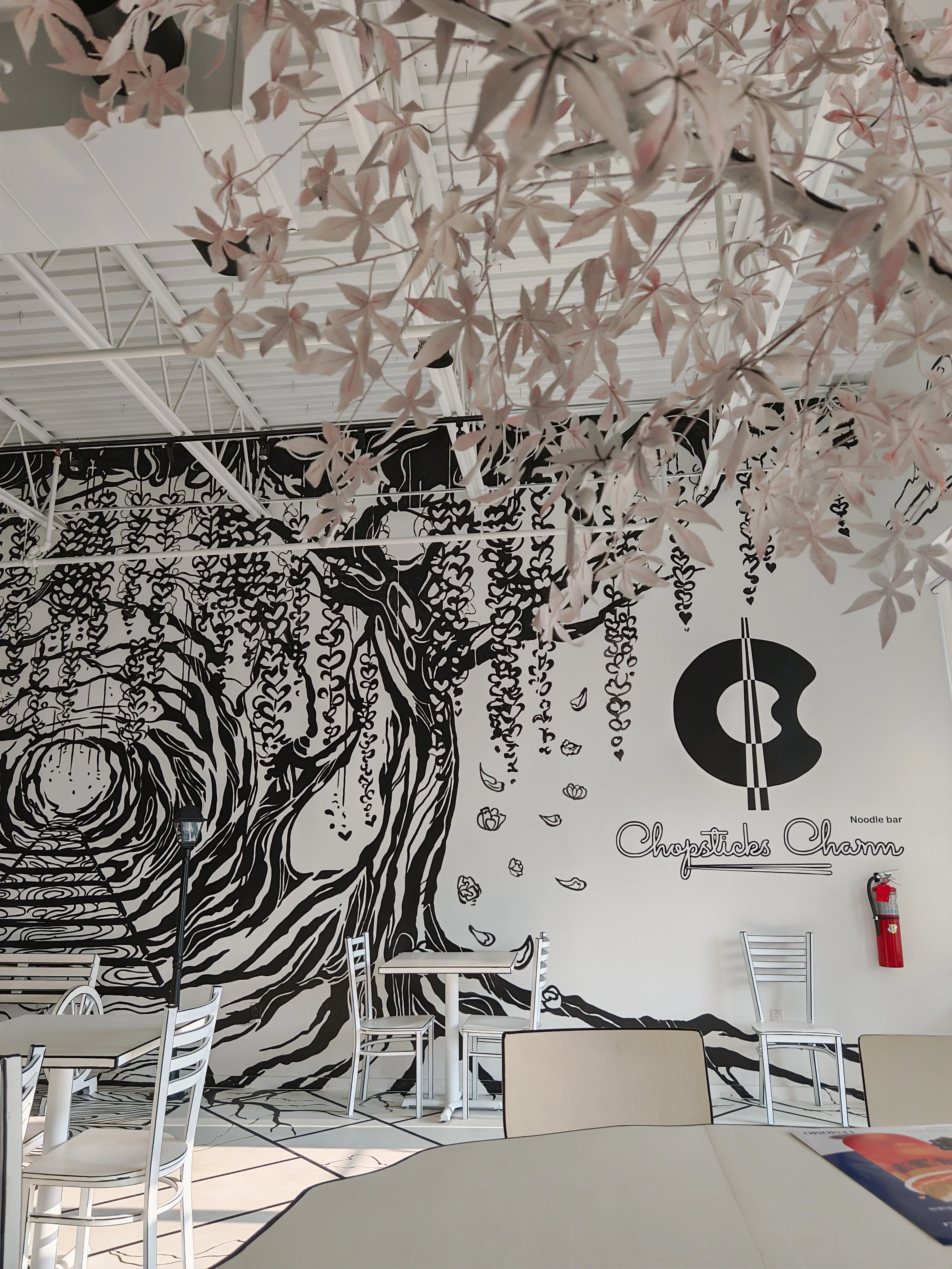 An immersive, black and white wall mural at Chopsticks Charm that creates an illusion of a path leading into a tunnel of trees, complete with a 2-D style bench.