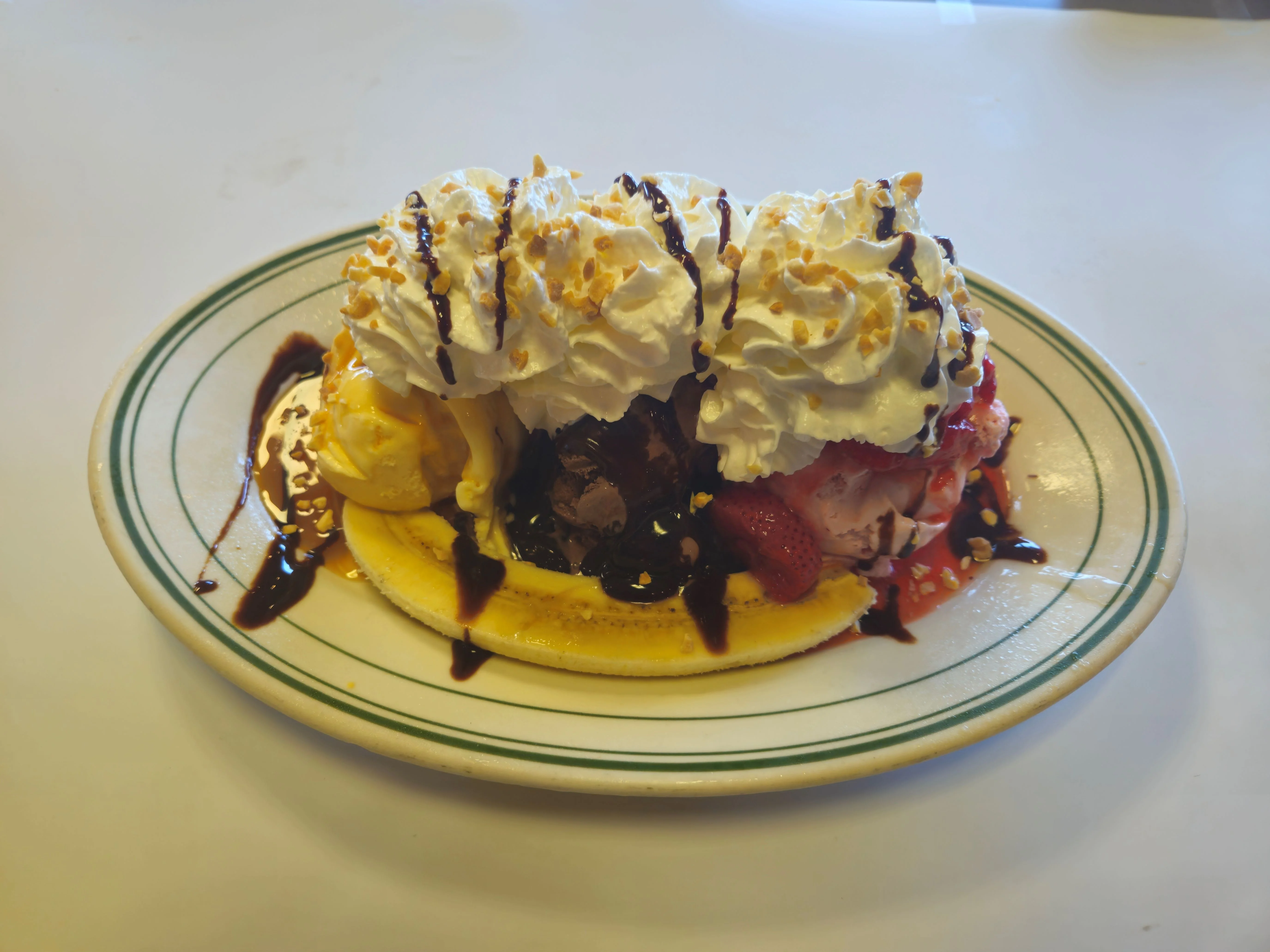 A delicious banana split topped with whipped cream, chocolate and strawberry sauces, and nuts, served in a white dish.