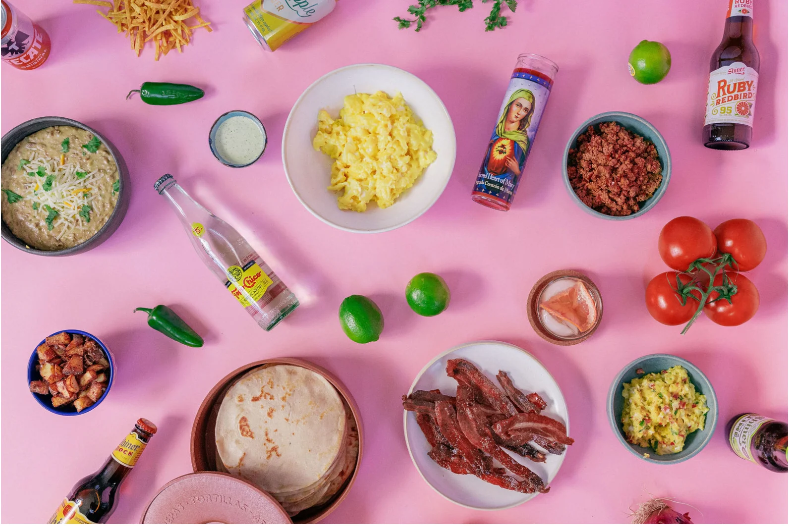 Colorful spread of Mexican breakfast dishes and ingredients on a pink background