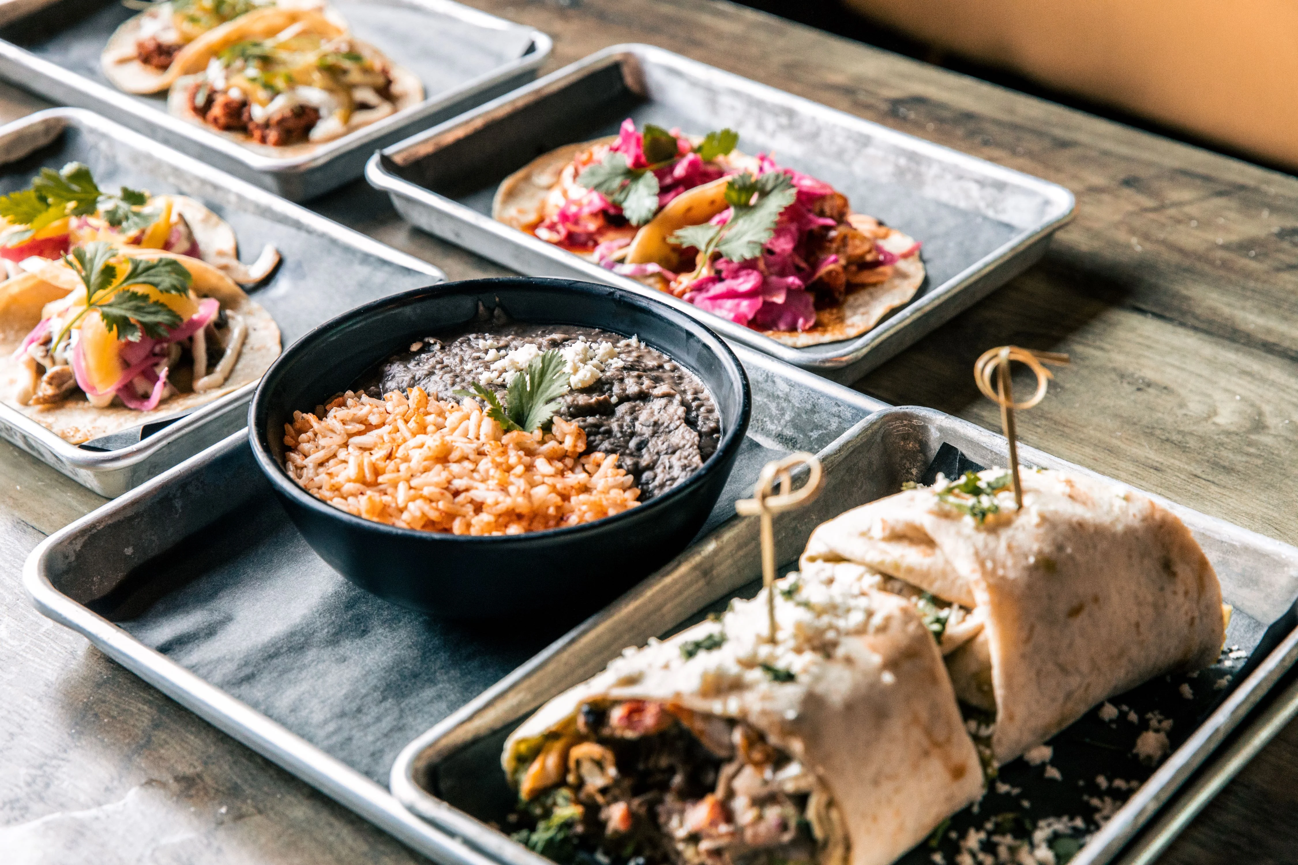 Mexican tacos with colorful garnishes, rice, and black beans on a restaurant buffet