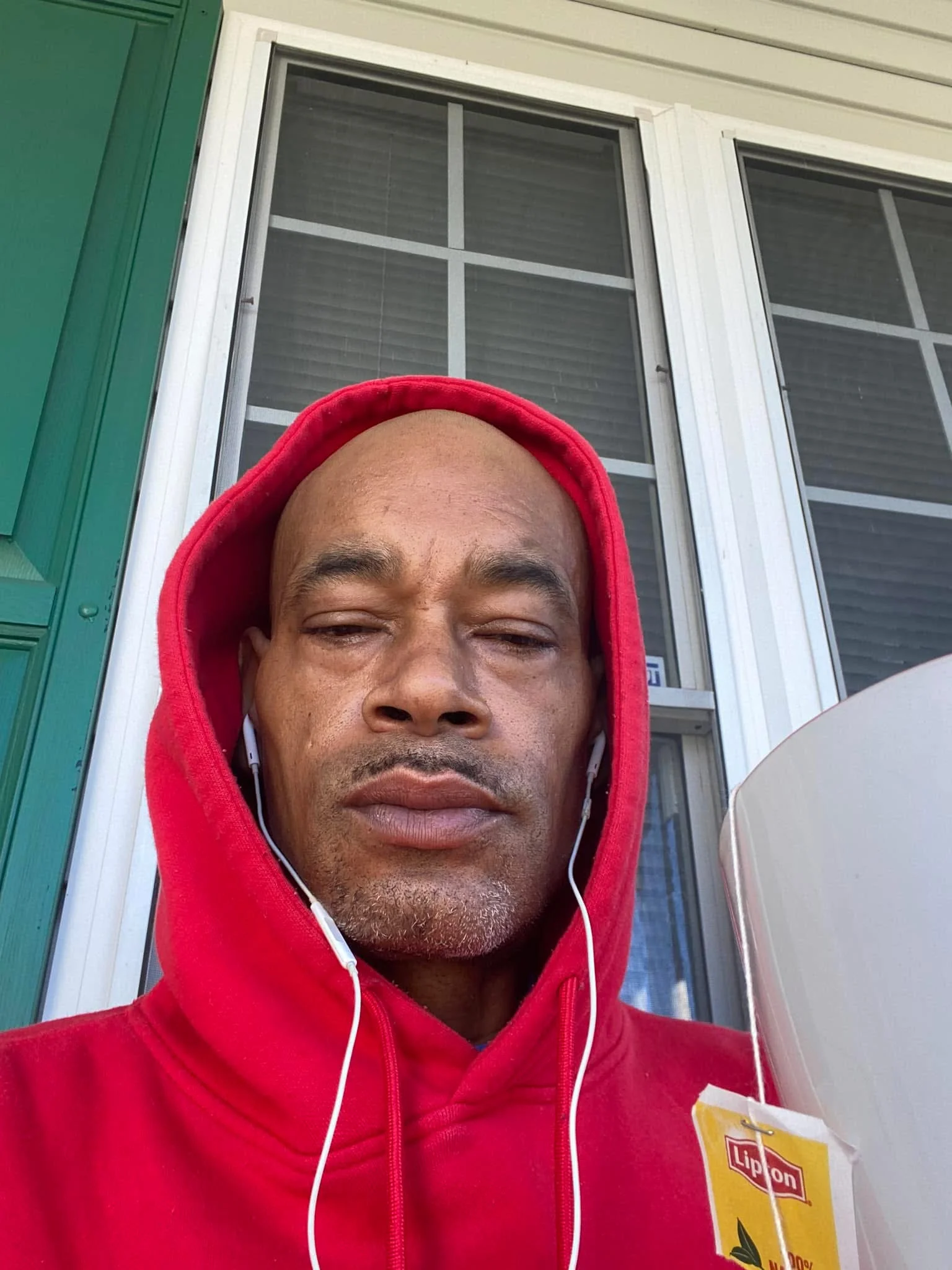 Man in a red hoodie enjoying tea on a porch