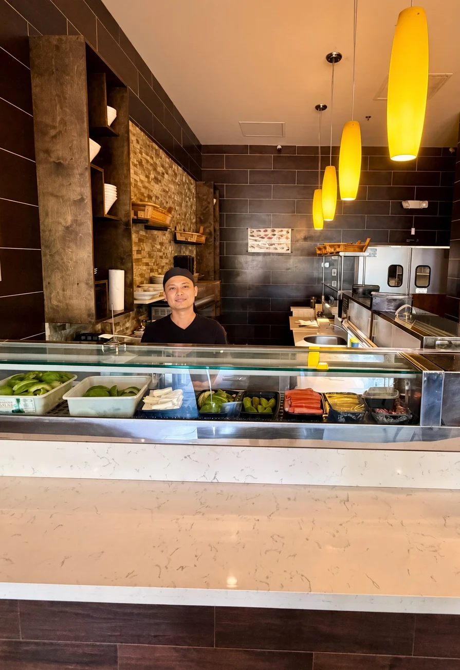 An interior view of a restaurant featuring a preparation area with fresh ingredients displayed in trays, and modern lighting.