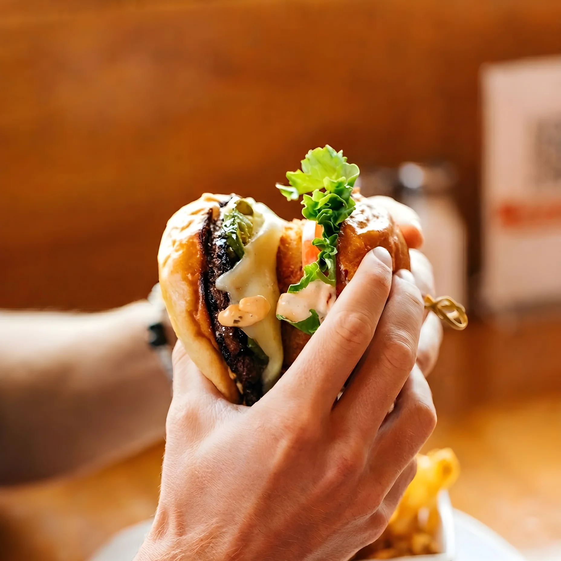 A hand holding a delicious burger with lettuce and sauce.
