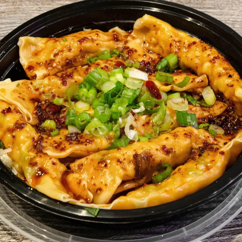 A bowl of dumplings topped with green onions and sauce.