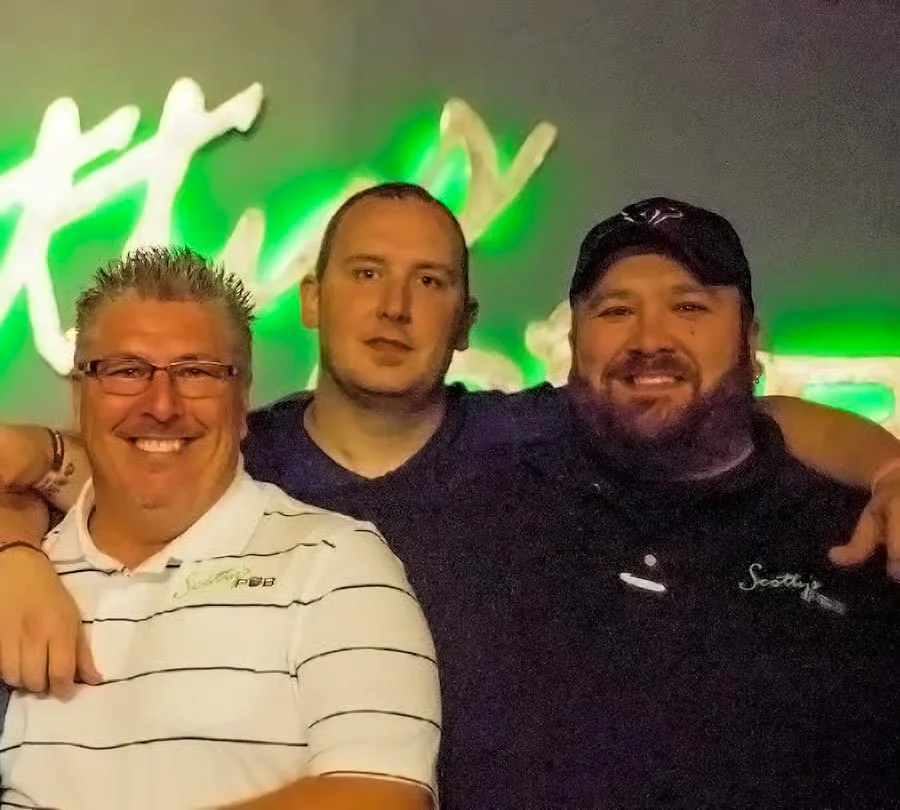 Three restaurant staff members posing together with a neon sign in the background