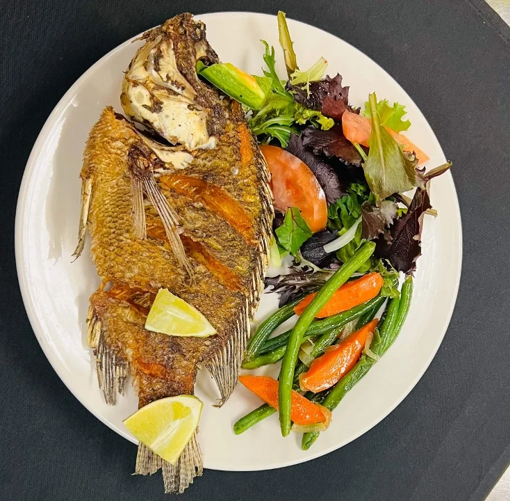 Crispy fried fish served with fresh green salad, tomatoes, and lime wedges on a white plate.