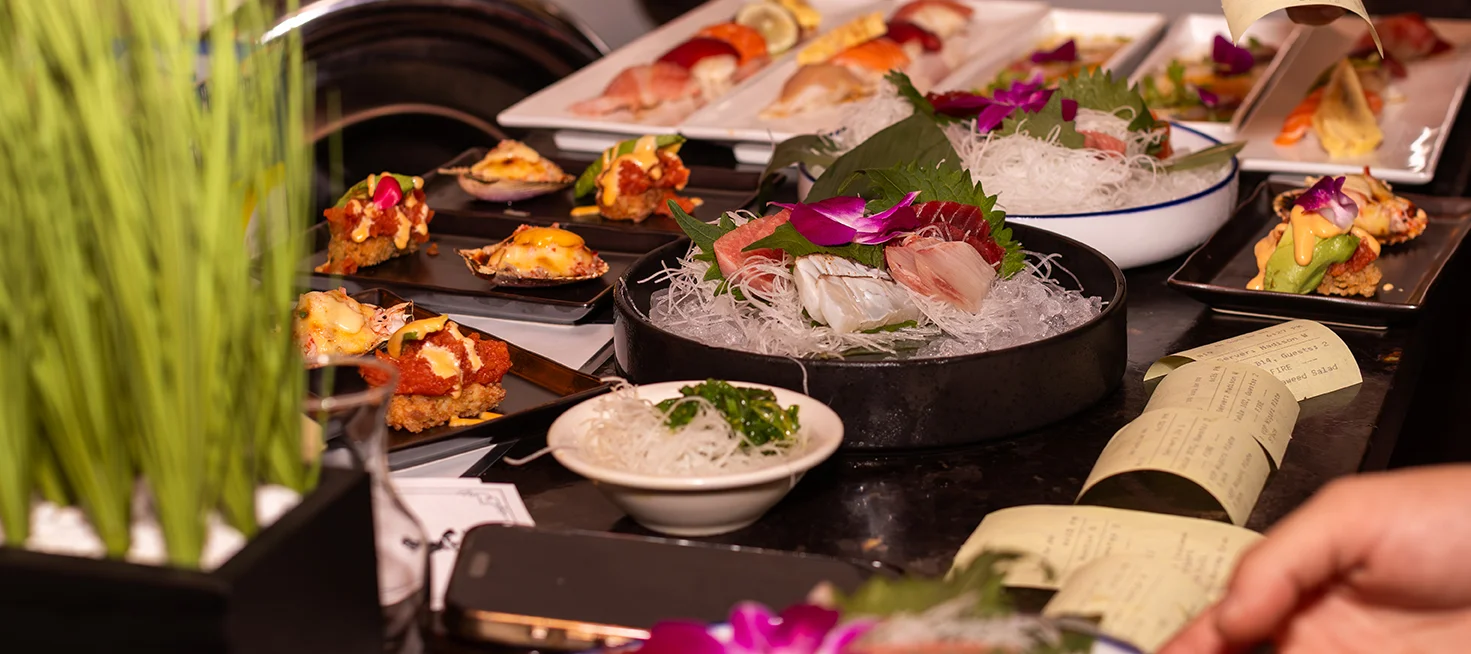 Elegant sushi and sashimi dishes arranged on plates with garnishes and a hand reaching for food