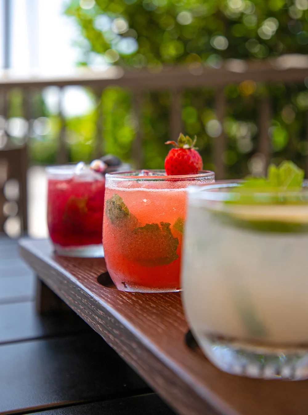 Colorful cocktails on a wooden tray in a sunny outdoor setting