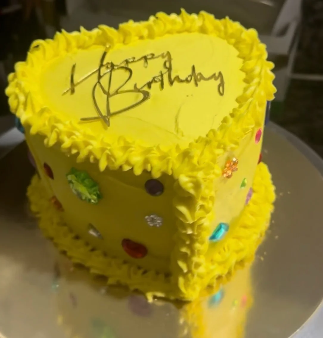 Bright yellow birthday cake in a heart shape with colorful decorations