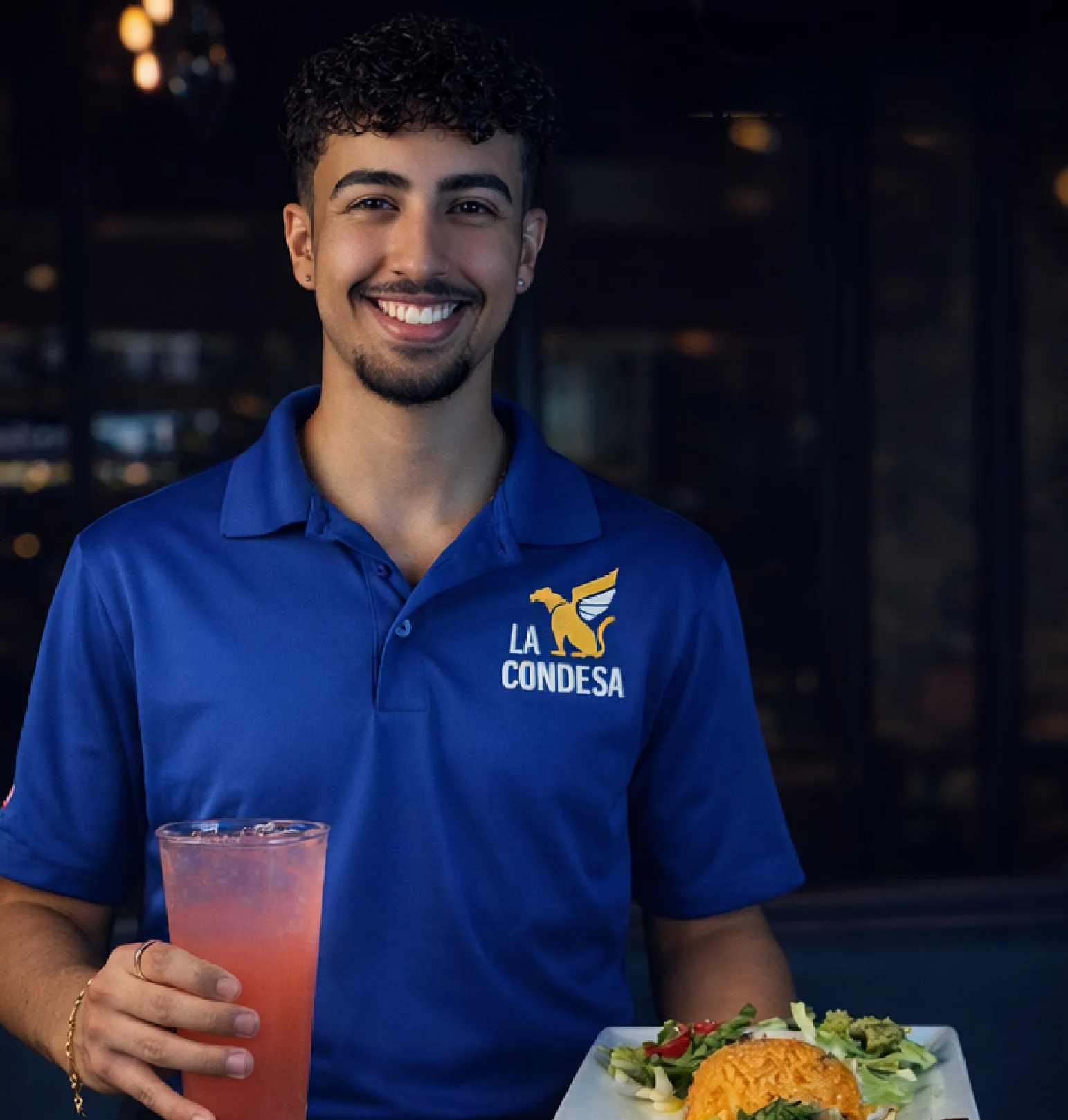 Smiling server holding a drink and a plate of food at La Condesa restaurant.