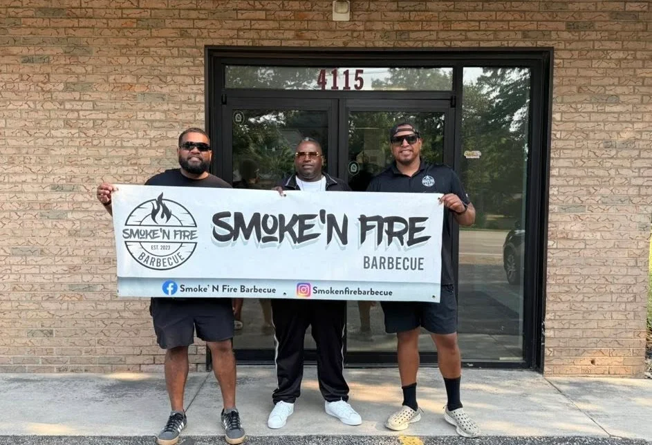 Team holding a banner for Smoke'n Fire Barbecue outside their restaurant