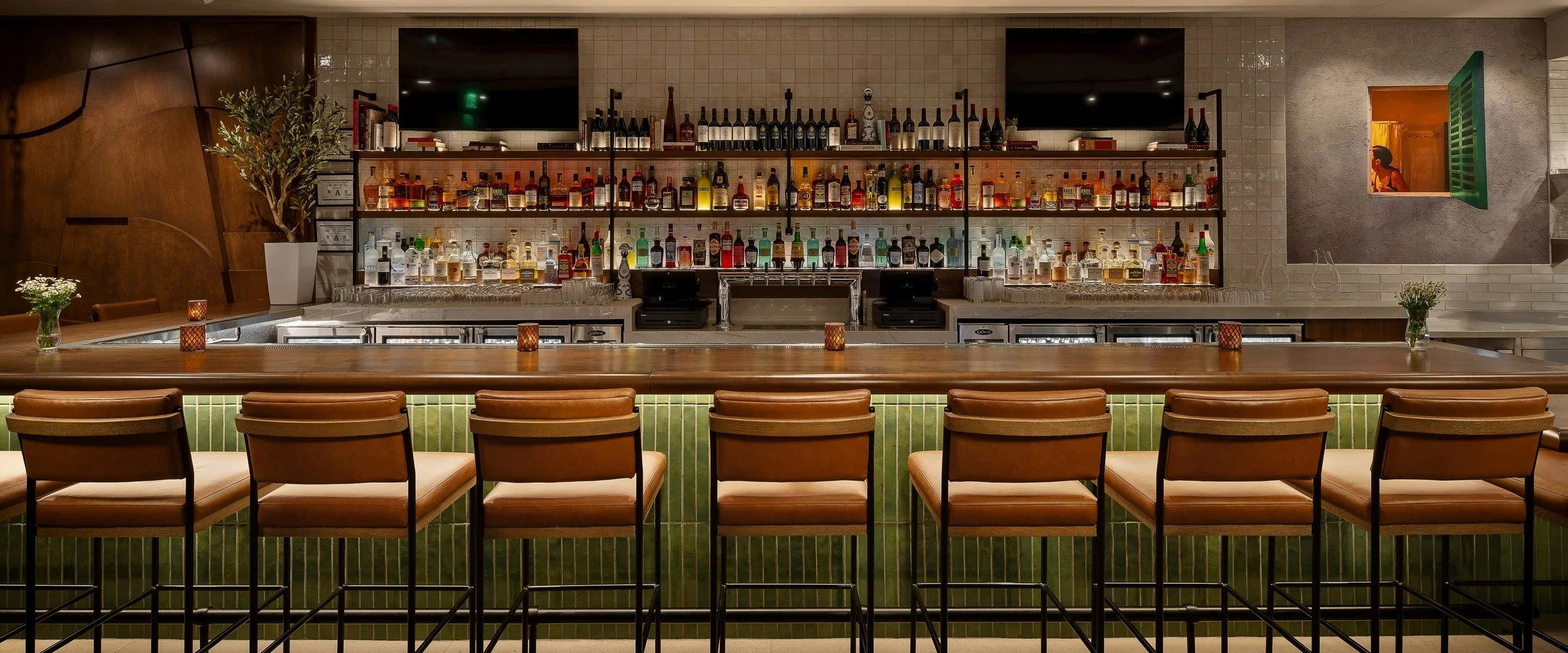 The bar at Nudo Italiano in Southern Highlands, Las Vegas, with leather stools along a green-tiled bar