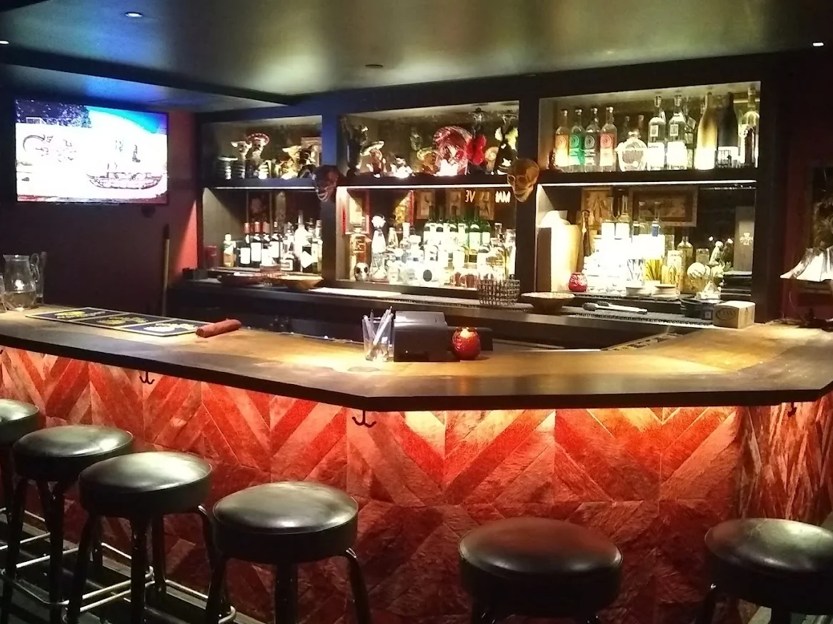 An intimate bar setting with wooden stools, a well-stocked back bar, and soft lighting creating a cozy atmosphere.