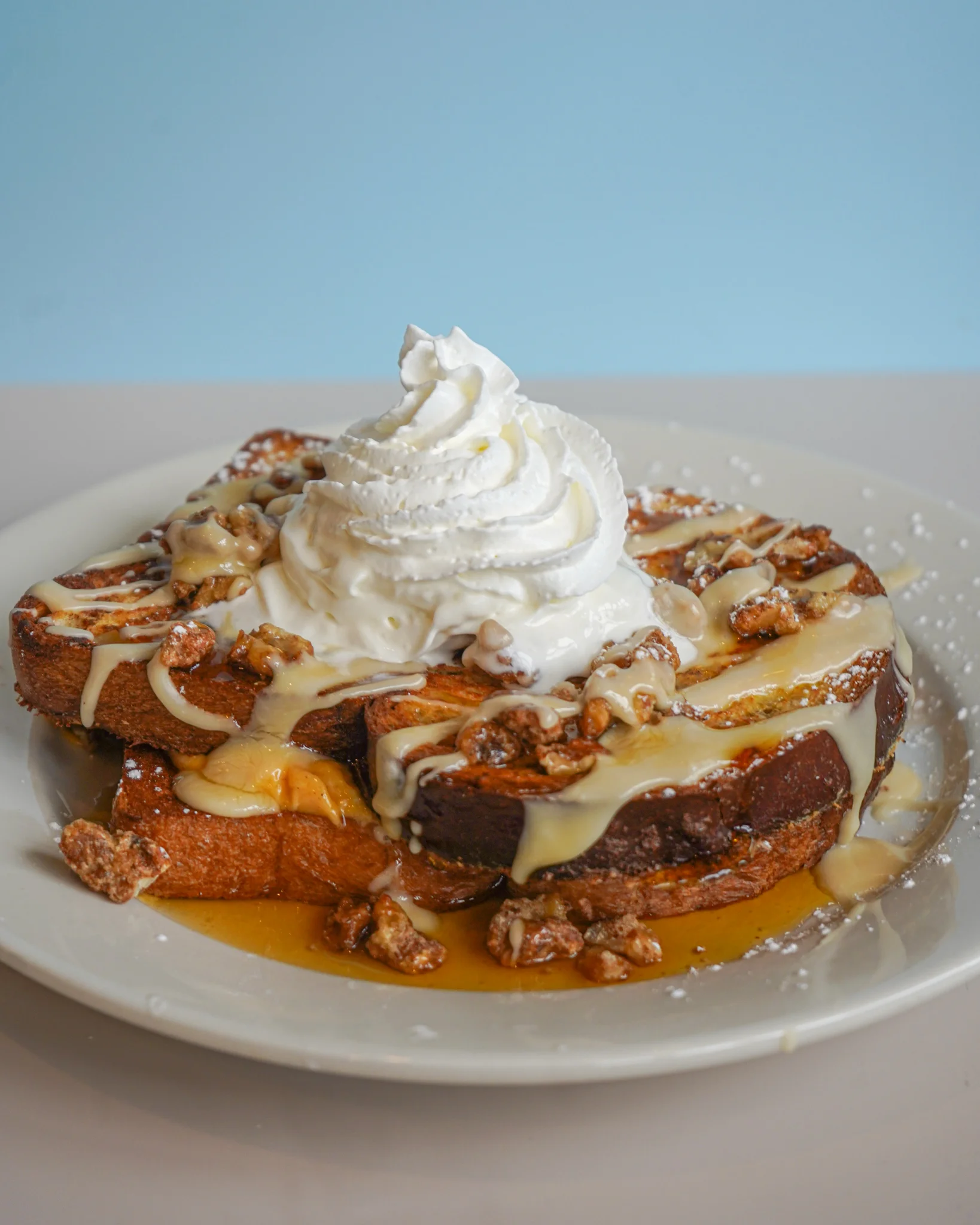 Thick slices of French toast topped with whipped cream, caramel drizzle, and crunchy toppings, served on a white plate.