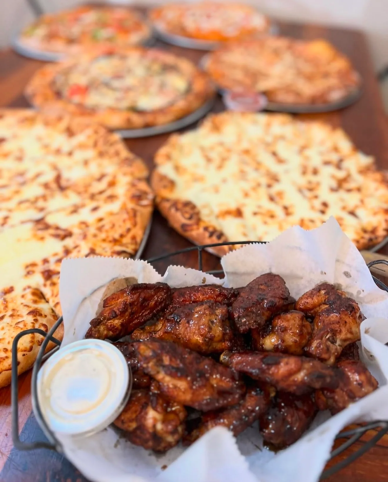 Crispy chicken wings with dipping sauce and pizzas in the background