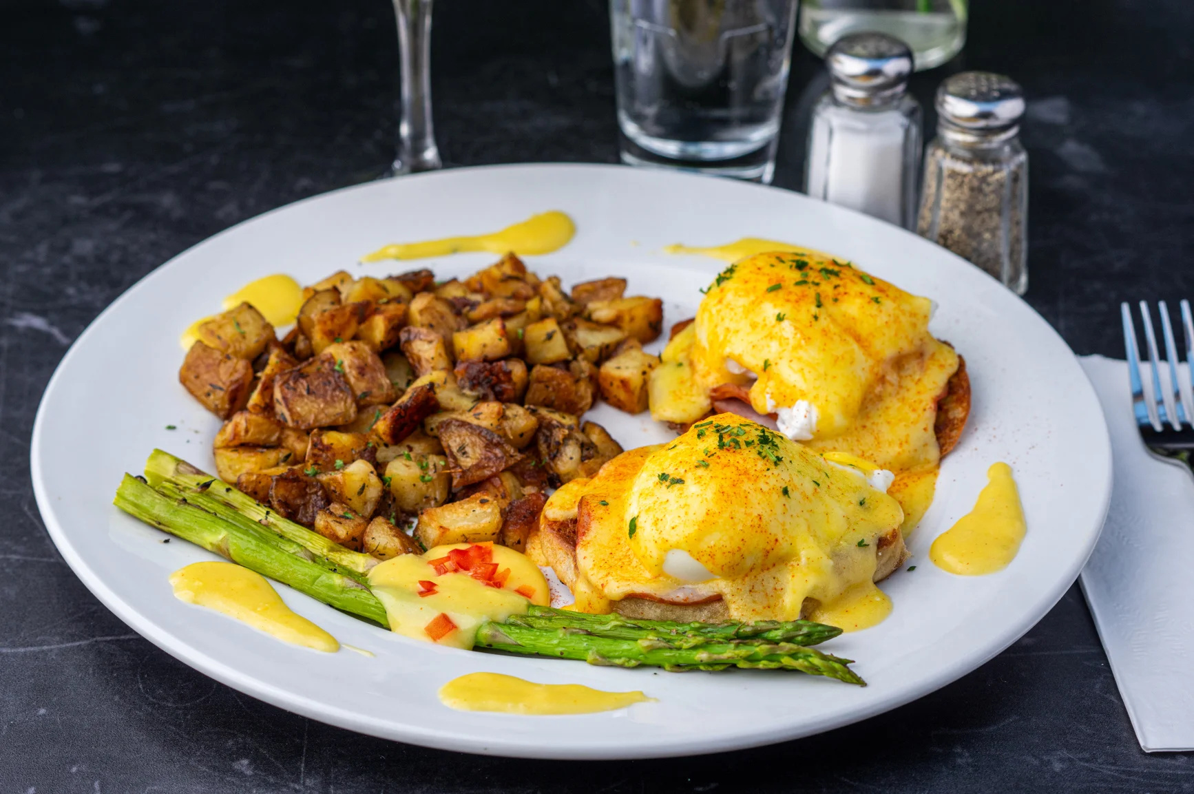 A plate of eggs Benedict and diced potatoes