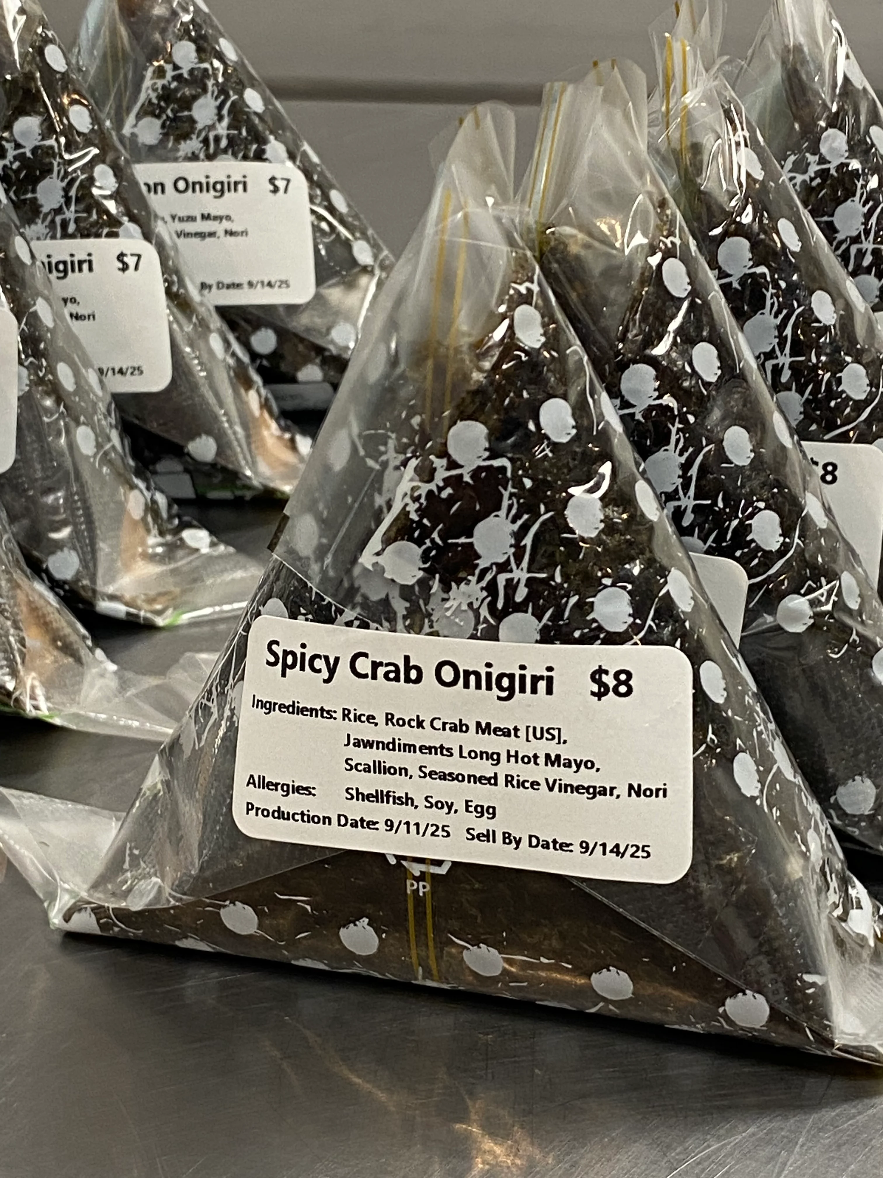 A packet of spicy crab onigiri, featuring a triangular shape and a clear label with ingredients and pricing information.