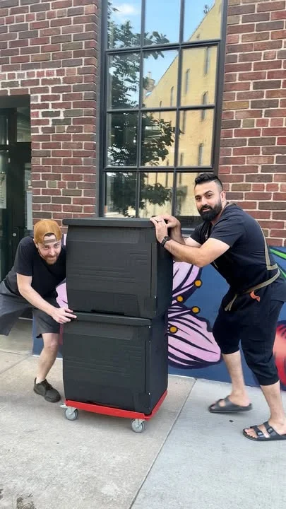 Two restaurant staff moving storage bins outside a brick building