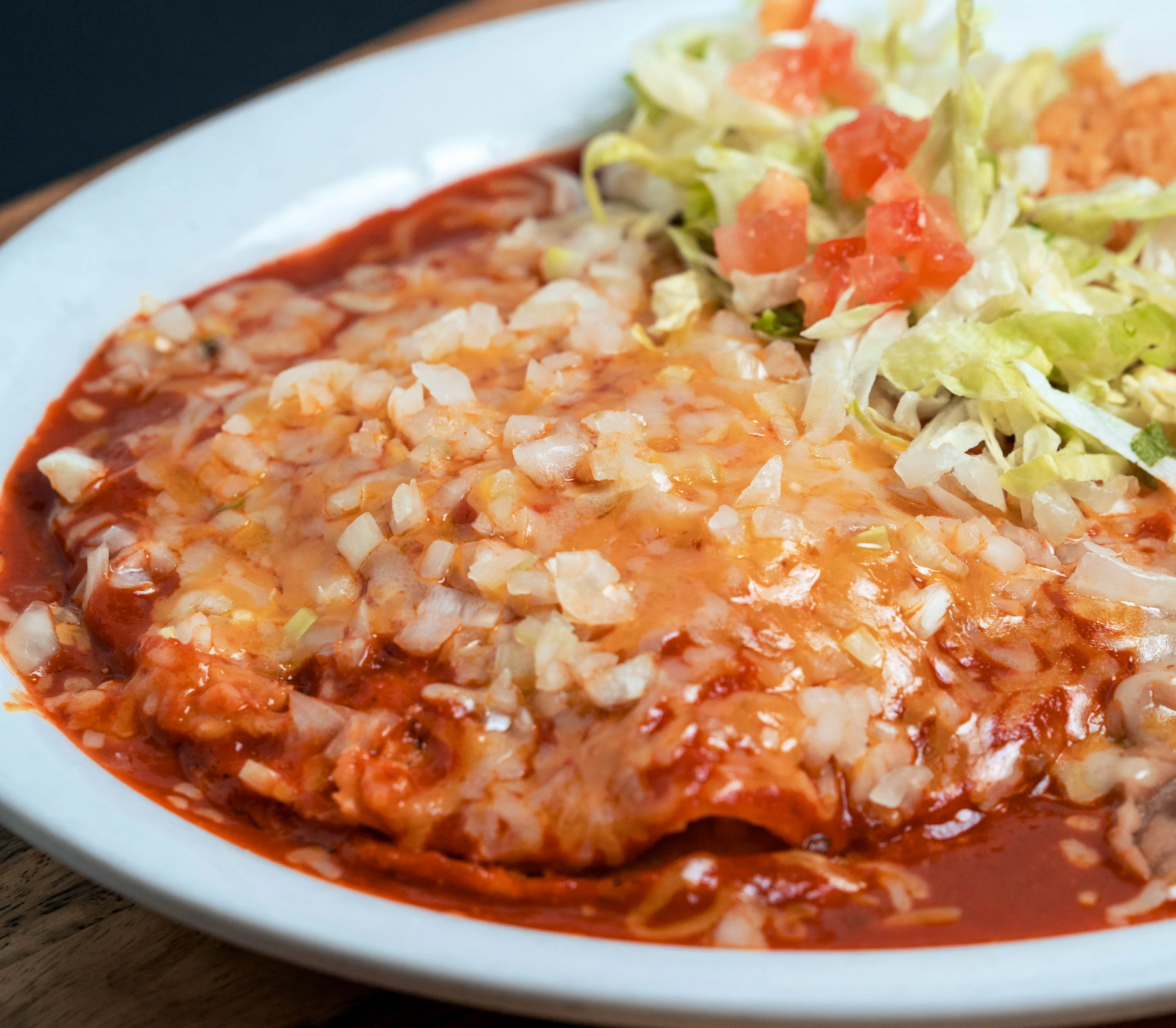 Plate of enchiladas topped with cheese and onions, served with rice and beans