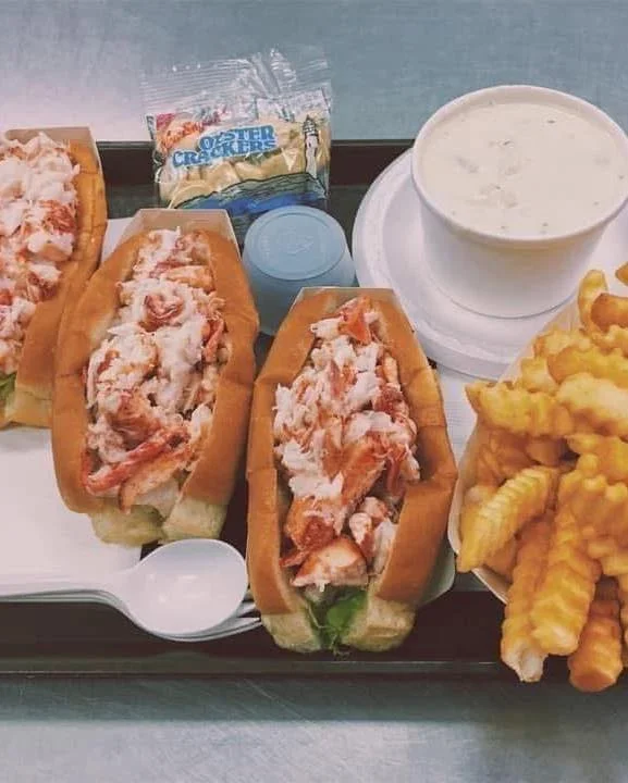 A tray featuring lobster rolls, a cup of clam chowder, crinkle fries, and a packet of crackers.