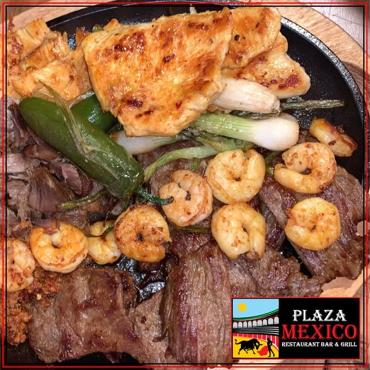 A sizzling plate featuring a mix of meats including steak and chicken, accompanied by shrimp and grilled vegetables. The dish is rich in flavor and ideal for a hearty meal.