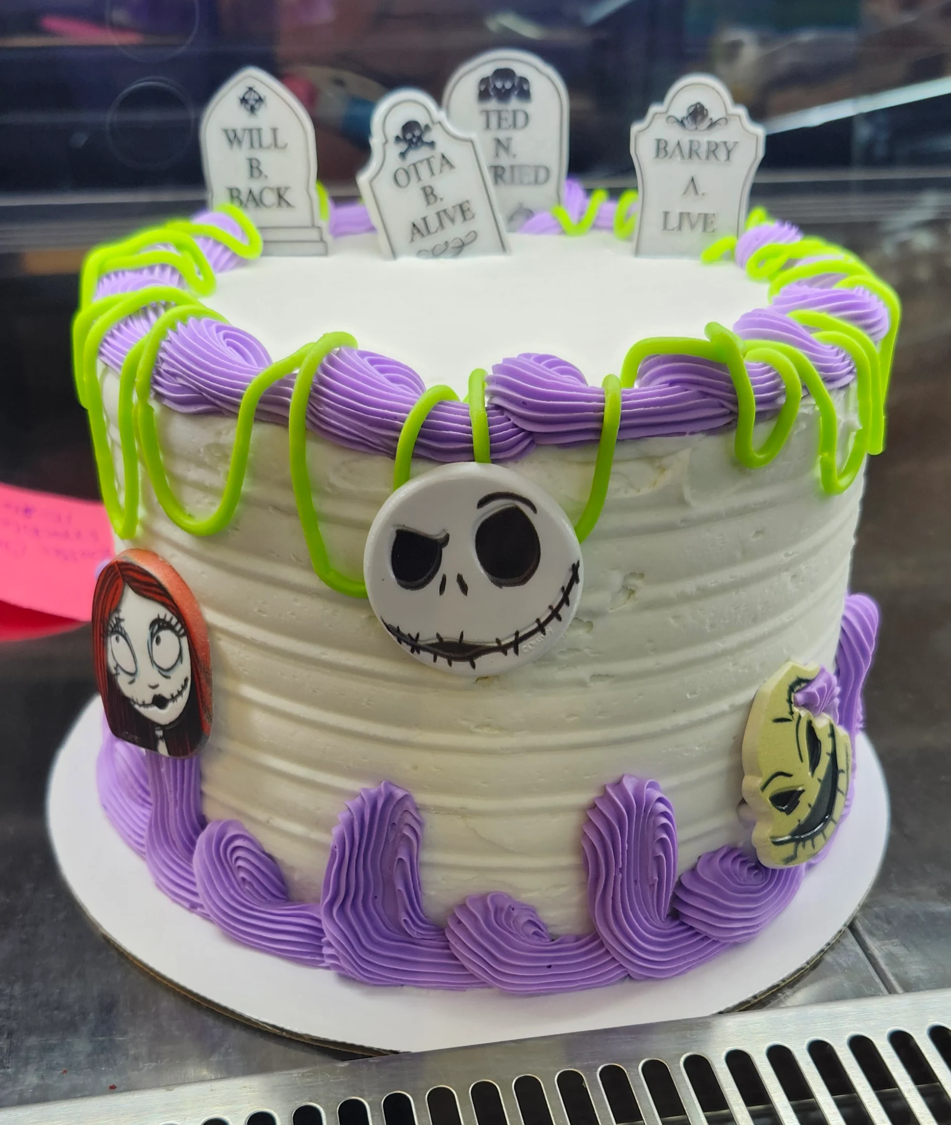 Small round cake with green & purple decorations and Nightmare Before Christmas characters & tombstones.