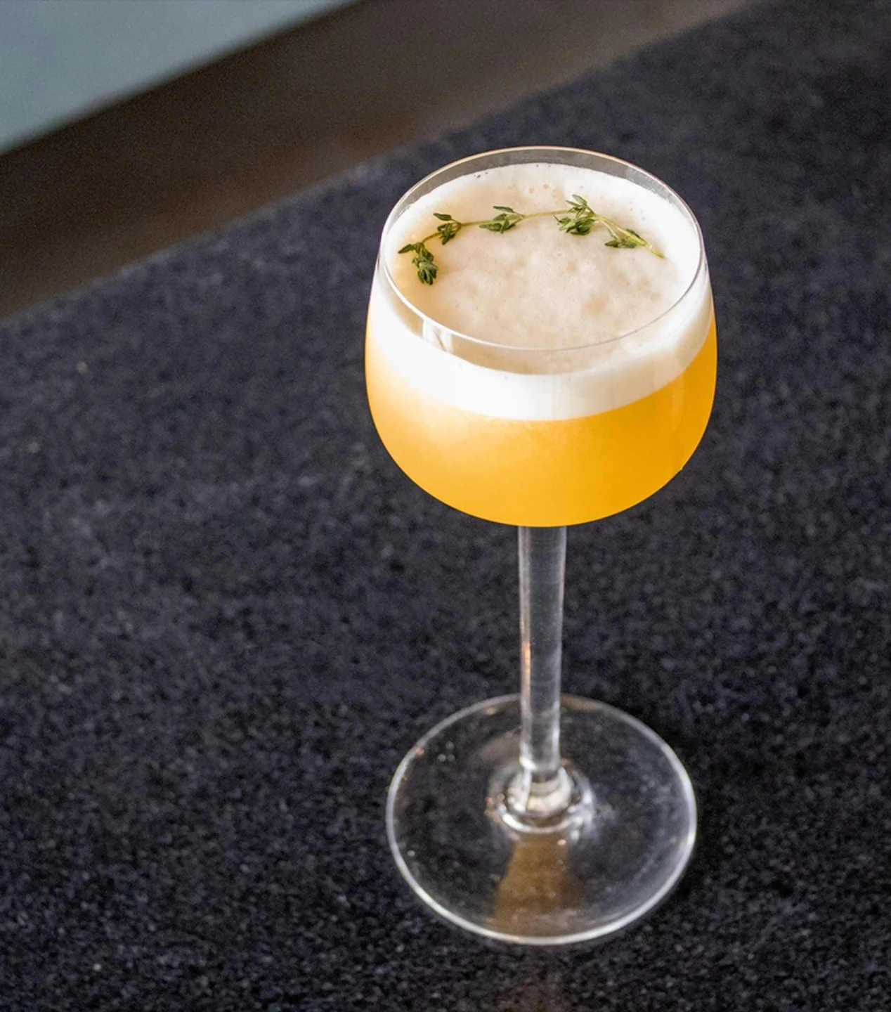 Craft cocktail with frothy top and thyme garnish in elegant glass