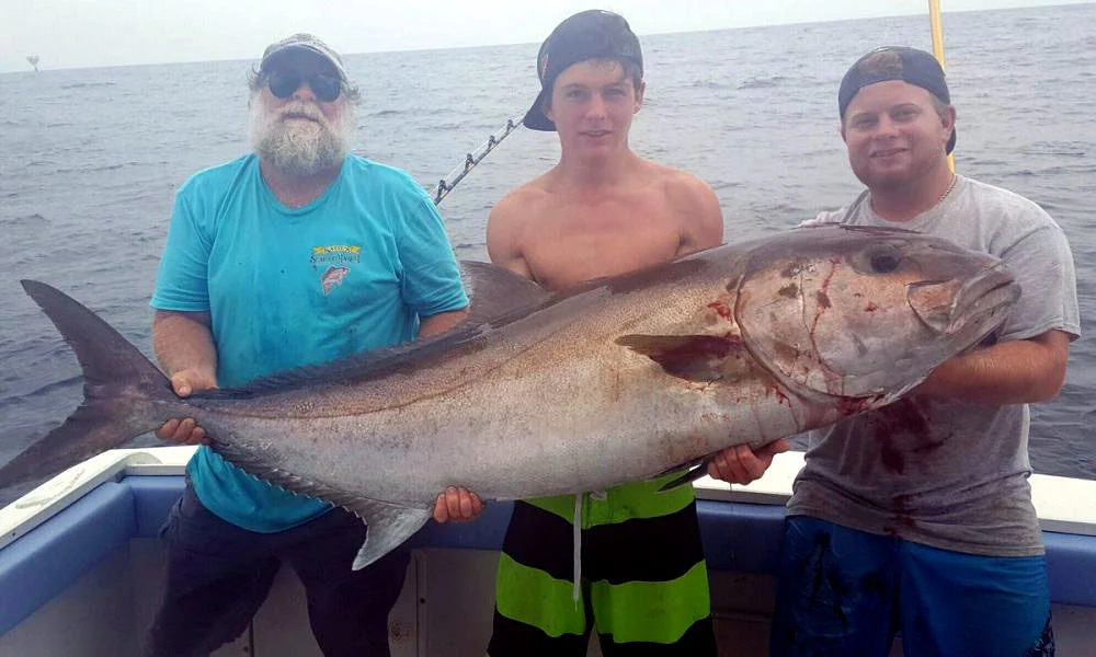 Three fishermen proudly holding a large fish at sea