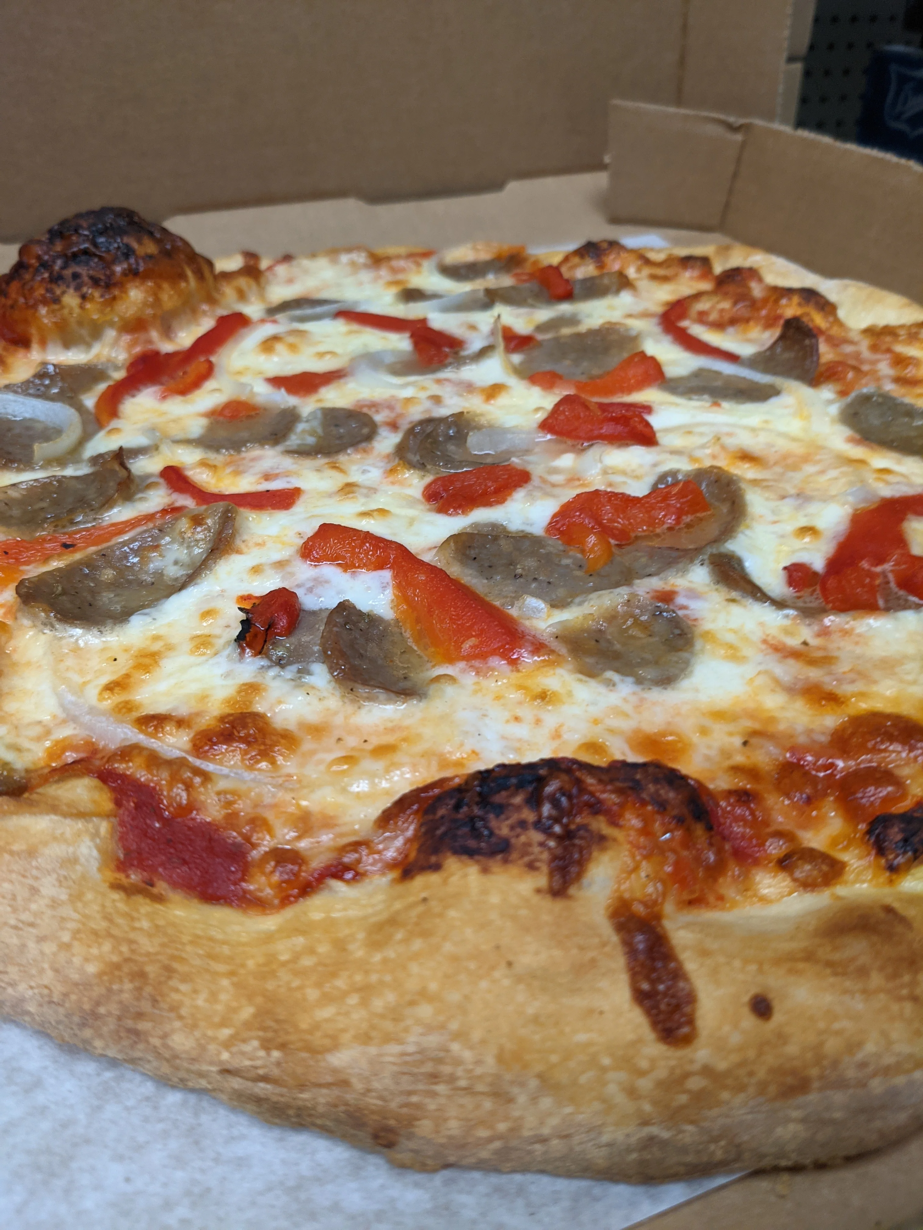 A pizza featuring sausage and red bell peppers on a golden crust.